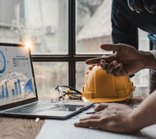 Man pointing at laptop on desk with construction hat and safety glasses.