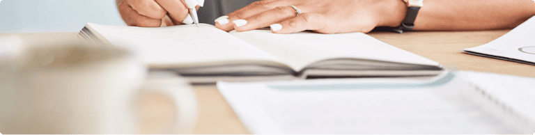 Woman writing in notebook on desk.
